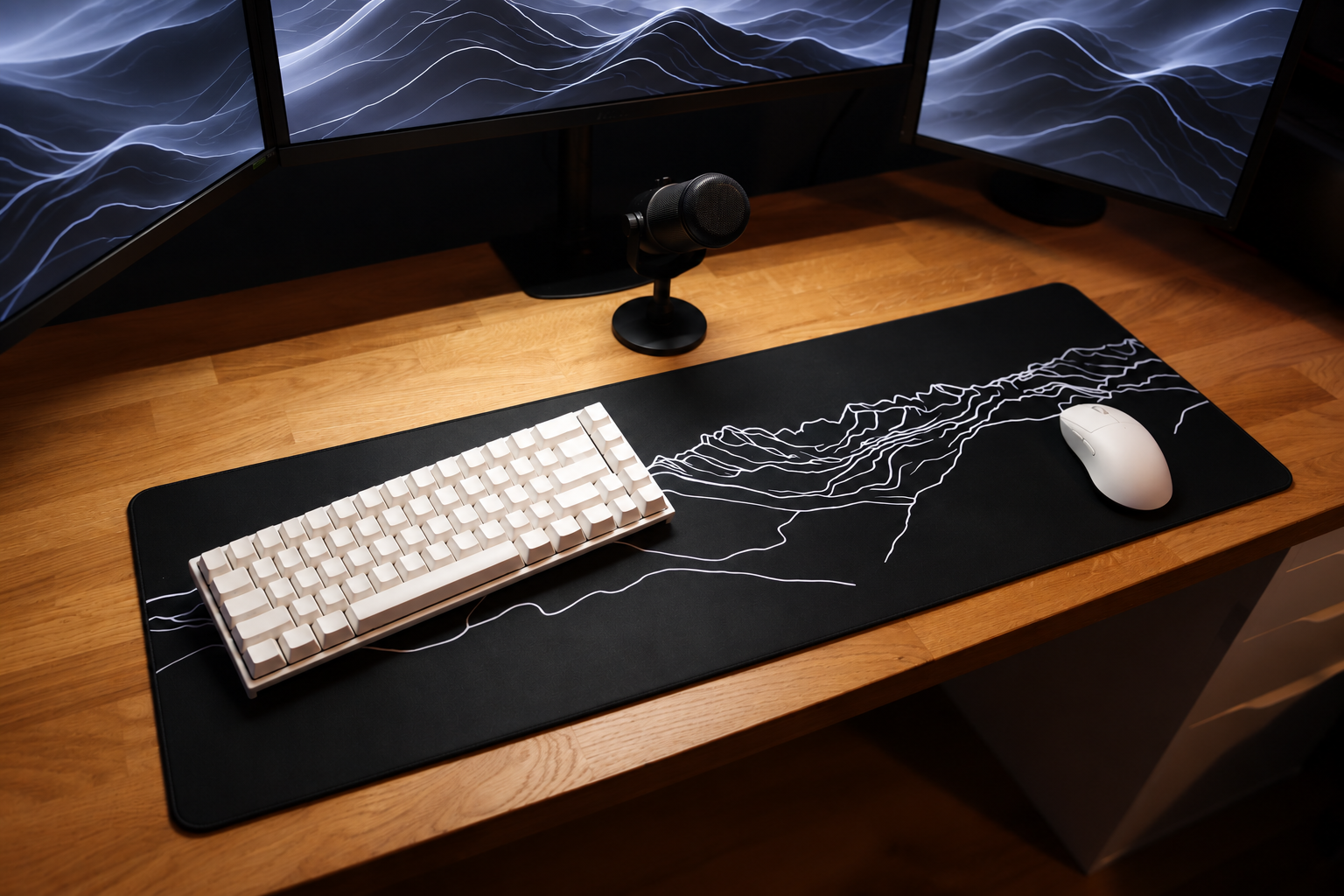 Dot2. black Mountain mousepad with white mountain line art on a wooden desk beneath a white keyboard and mouse.